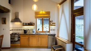 A modern kitchen with wooden cabinets, a gas stove, and a window with blinds. - The Two Arches - Les Arches de Muschamp - Holiday Homes with Style & Comfort (Cussay, Centre-Val De Loire)