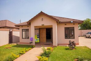 A single-story building with a 'BAR' sign above the entrance, a small front garden, and a parked car in the background. - Minachi Exclusive Lodge (Lusaka)