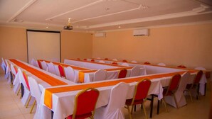 Une salle de conférence avec des rangées de tables, chacune recouverte d’une nappe blanche et agrémentée d’un chemin de table orange, ainsi que des chaises rouges aux pieds dorés.