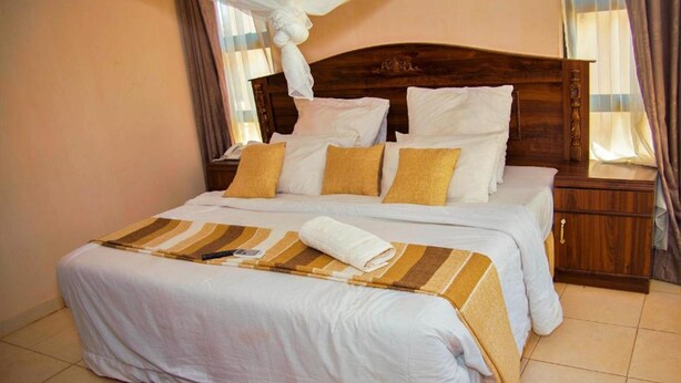 Un lit double avec une literie blanche et beige, une tête de lit en bois, une table de chevet avec une lampe et un tapis à motifs sur le sol.