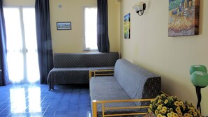 Een woonkamer met een bank, een eettafel met een mand vol bloemen, en een schilderij aan de muur.