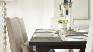 A dining area with a dark wooden table, white chairs, and a modern abstract painting on the wall.