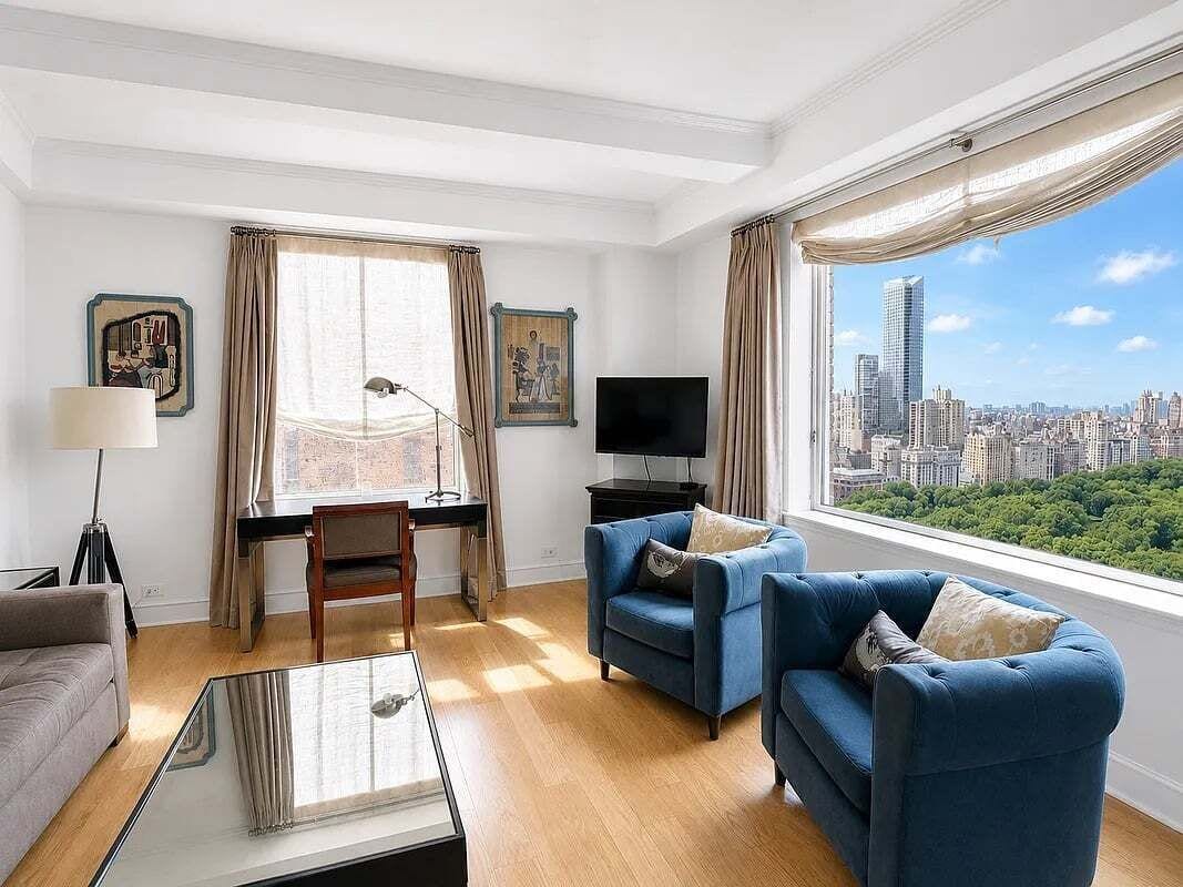A modern living room with a city view, a desk with a computer, and a flat-screen TV.