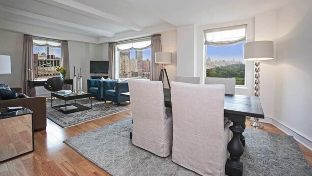 A modern hotel room with a city view, a flat-screen TV, a dining area with a table and chairs, and a large window with curtains.