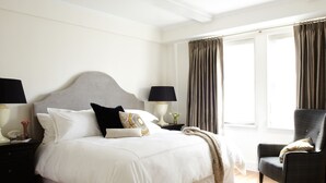 A neatly arranged bedroom with a large bed, two bedside tables with lamps, a chair, and a window with curtains.