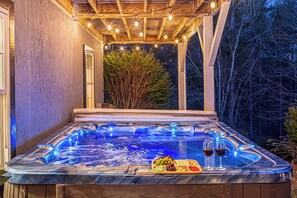 Un jacuzzi con muelle de madera, rodeado de árboles y luces colgantes.