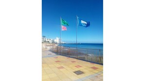 Une promenade en bord de mer avec une allée dallée, une rambarde en métal et deux drapeaux sur des mâts.