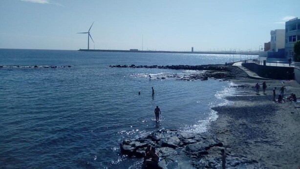 Un paysage côtier avec une rive rocheuse, un pont au loin et des éoliennes.