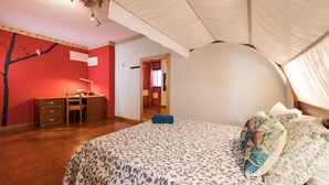 Une chambre à coucher avec un lit à baldaquin, un bureau et un mur rouge orné d’une fresque représentant un arbre.