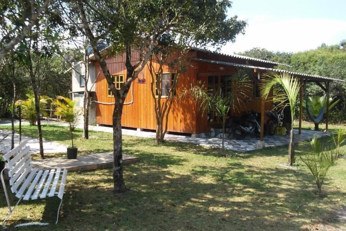 Una casa de madera con un porche, rodeada de árboles y un patio cubierto de césped.