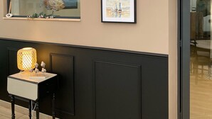Un intérieur moderne avec un mur de couleur beige, deux œuvres d’art encadrées, une sculpture de poisson décorative et une table avec une lampe.