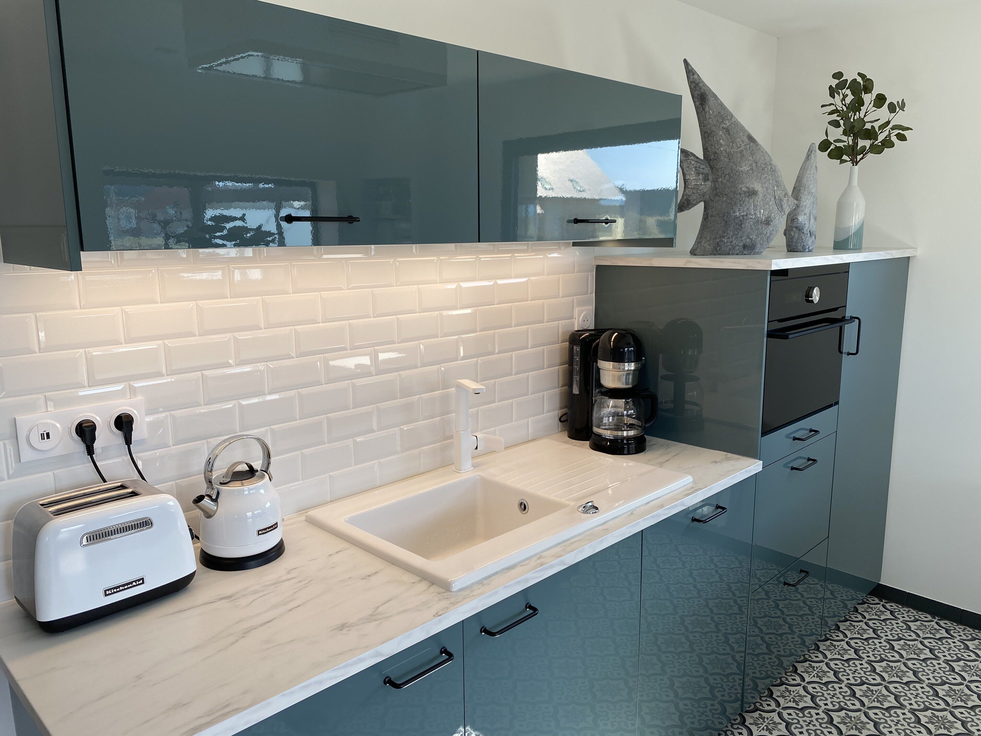 A modern kitchen with a white tiled backsplash, a marble countertop, a coffee maker, a toaster, and a sink.