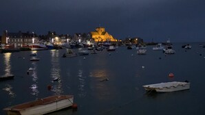 Un port au crépuscule, avec des bateaux amarrés et, au fond, un bâtiment imposant coiffé d’un toit jaune.