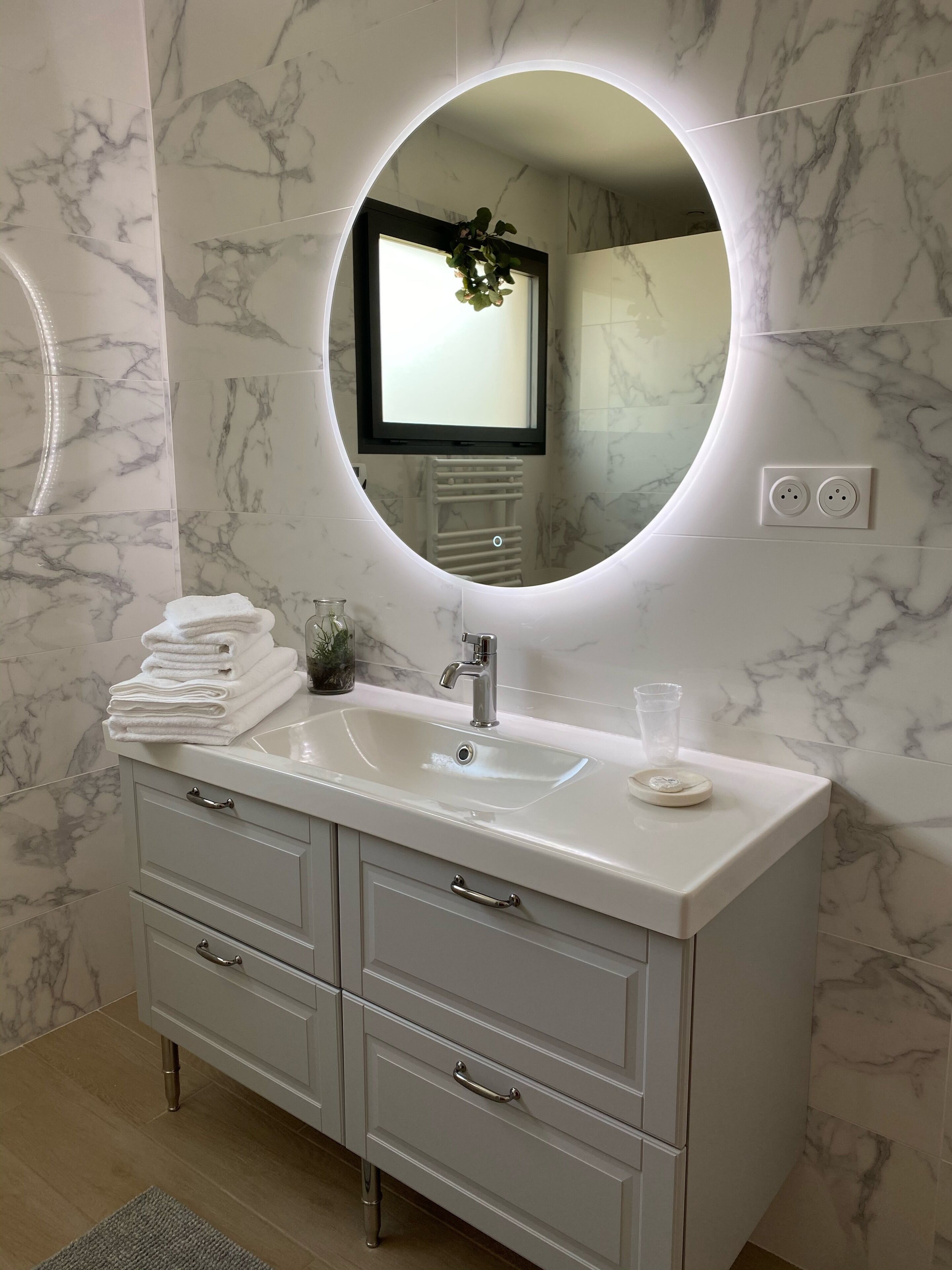 A bathroom with a marble vanity, a round mirror with a light, and a sink.