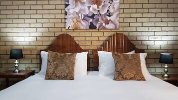 Habitación de hotel con pared de ladrillo, cabecero de madera, dos camas blancas con almohadas marrones estampadas y dos lámparas de noche.