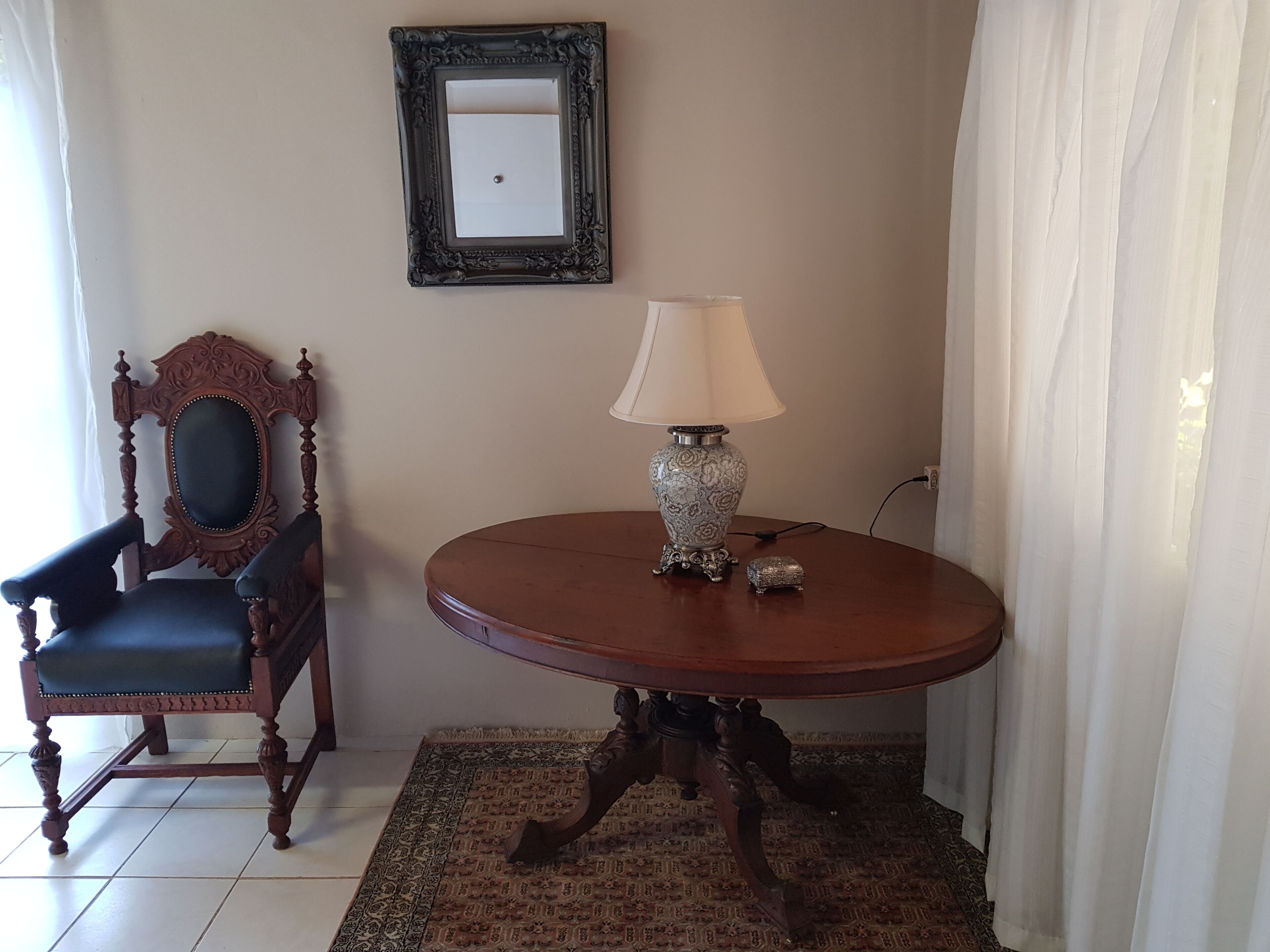 Una habitación con una mesa redonda de madera, una silla, una lámpara y un espejo en la pared.