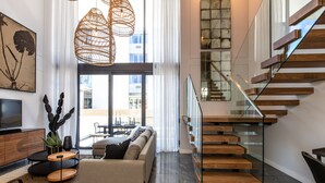 A modern living room with a sofa, coffee table, and a TV. There is a staircase with glass railings and wooden steps. - Bradway Apartments (Cape Town)