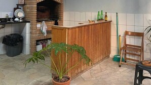 A kitchen with a brick oven, a wooden counter, a trash bin, a potted plant, and a broom.