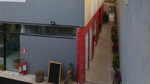 A modern building with a grey facade and red accents, featuring a narrow pathway with potted plants.
