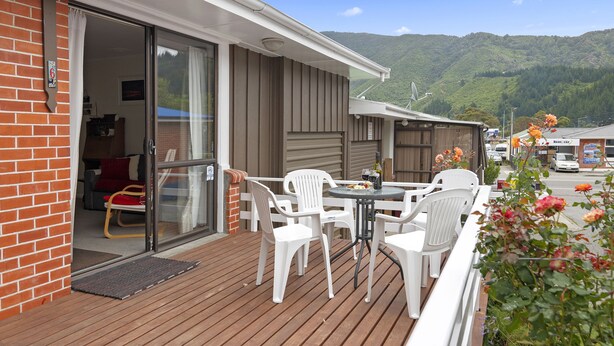 A balcony with a wooden deck, white plastic chairs, and a table with a bottle and fruit. - The Picton Family Retreat - Picton Unit (Picton)