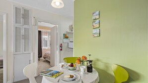 A dining area with a table set for two, a white chair, a green chair, and a bookshelf in the background. - The Picton Family Retreat - Picton Unit (Picton)