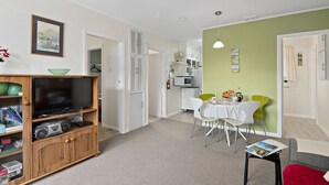 A living room with a TV, wooden entertainment unit, and a dining area with a table and chairs. - The Picton Family Retreat - Picton Unit (Picton)