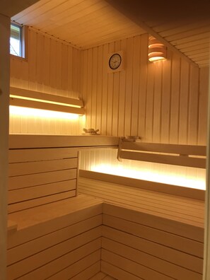 A sauna with wooden benches, a wall-mounted clock, and overhead lighting.