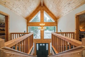 Un intérieur en bois avec un plafond haut, un lustre et une vue dégagée grâce à de grandes fenêtres.