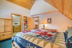Une chambre avec un grand lit, une armoire en bois, des étagères ouvertes remplies de livres et un ventilateur de plafond.