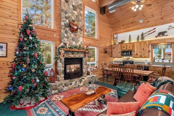 Un intérieur de chalet chaleureux avec une cheminée en pierre, un sapin de Noël et un coin repas.