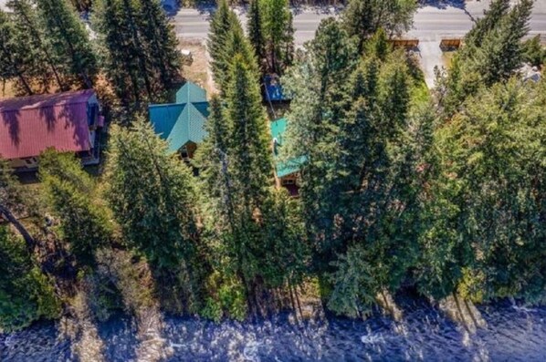 An aerial view of a forested area with a small building with a green roof, surrounded by dense trees.