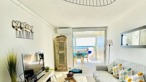 Un salon moderne avec un téléviseur, un canapé, un pouf et une vue sur l’extérieur.
