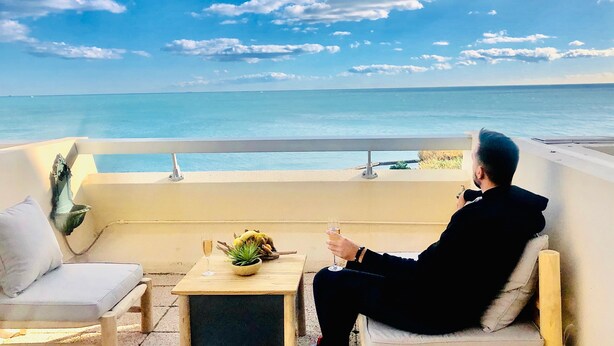 Une personne assise sur un balcon, d’où l’on a une vue sur la mer.