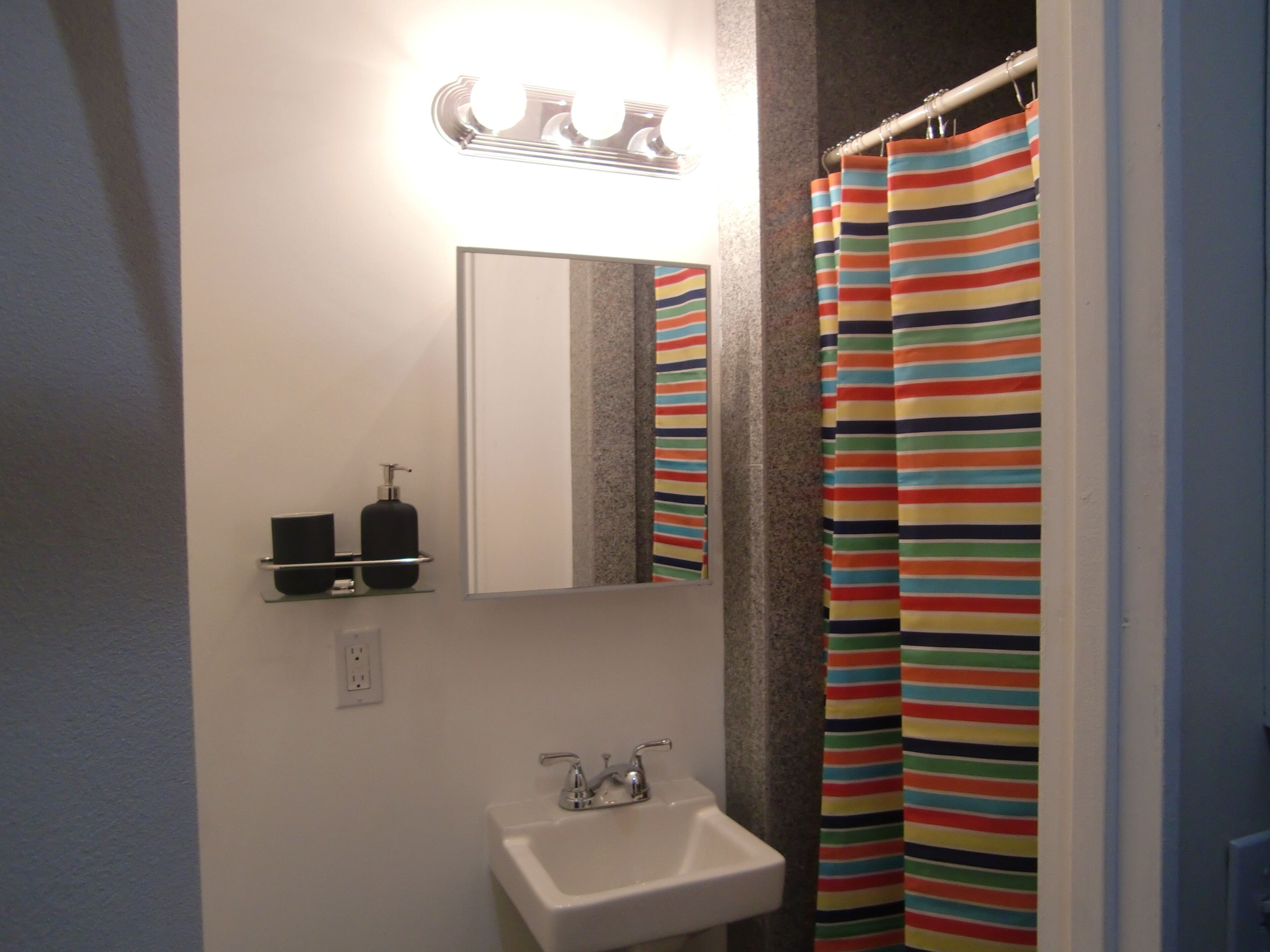 A bathroom with a white sink, a mirror, and a striped shower curtain.
