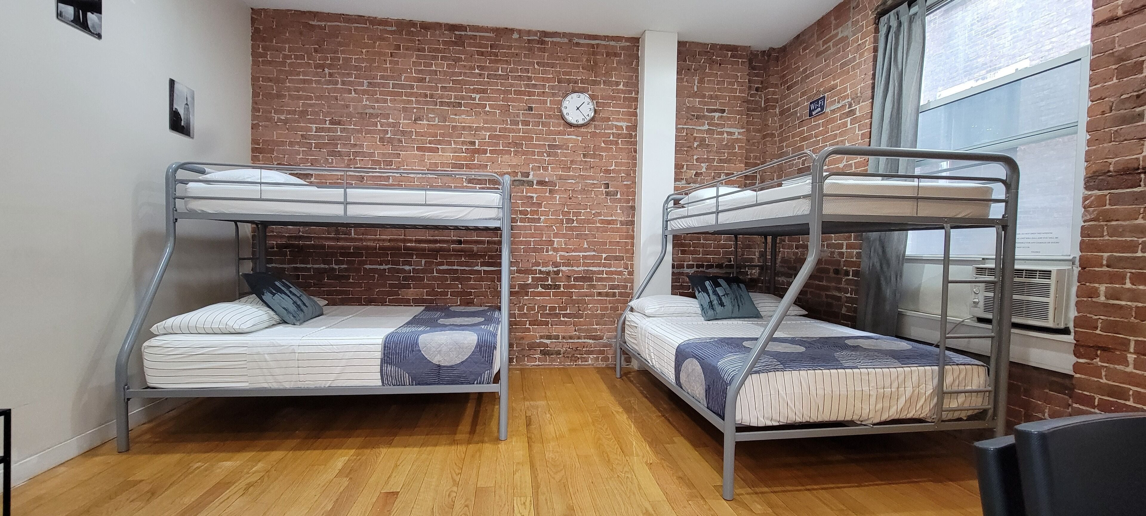 Une chambre de dortoir avec deux lits superposés, un mur en briques, une horloge et un appareil de climatisation.