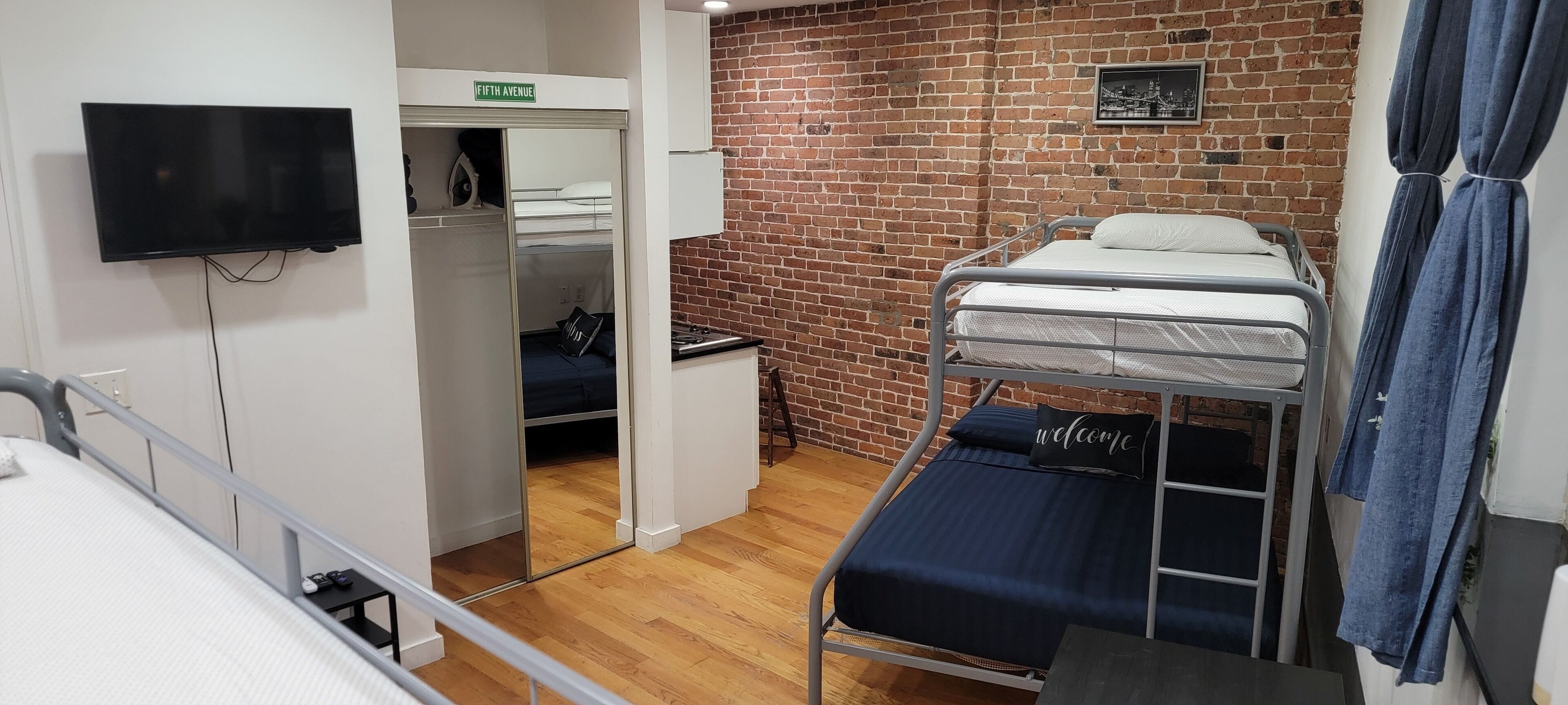 Una habitación tipo dormitorio con literas, un televisor, una pared de ladrillo y una almohada con la palabra 'Welcome'.