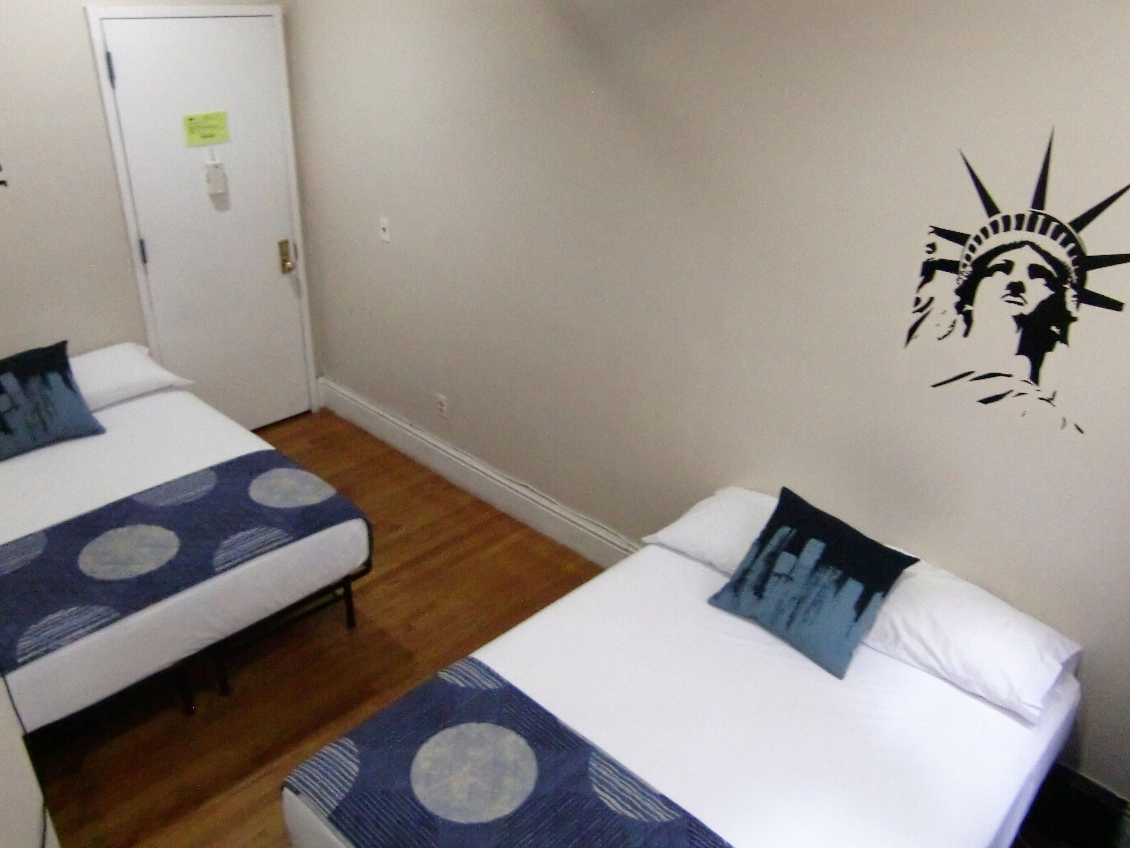 A hotel room with two beds, each with a patterned bedspread and pillows, a wooden floor, and a wall with a mural of the Statue of Liberty.