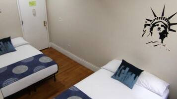 A hotel room with two beds, each with a patterned bedspread and pillows, a wooden floor, and a wall with a mural of the Statue of Liberty.
