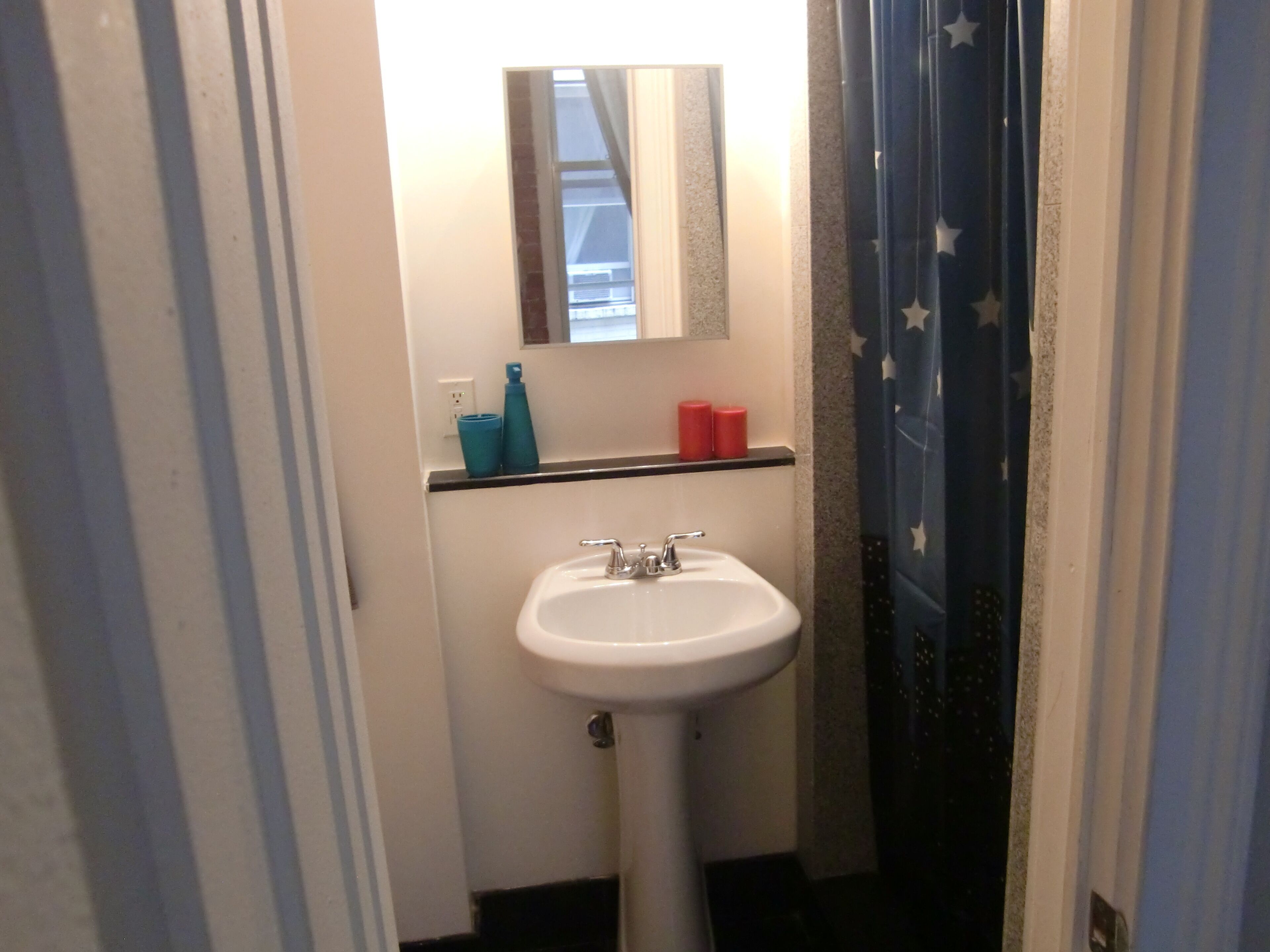 Een badkamer met een witte wastafel, een spiegel erboven en een plank met toiletartikelen.