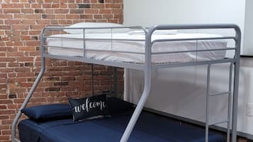 Ein Etagenbett mit Metallgestell und blauer Bettwäsche, eine Ziegelwand mit einem gerahmten Bild und ein Holzboden.