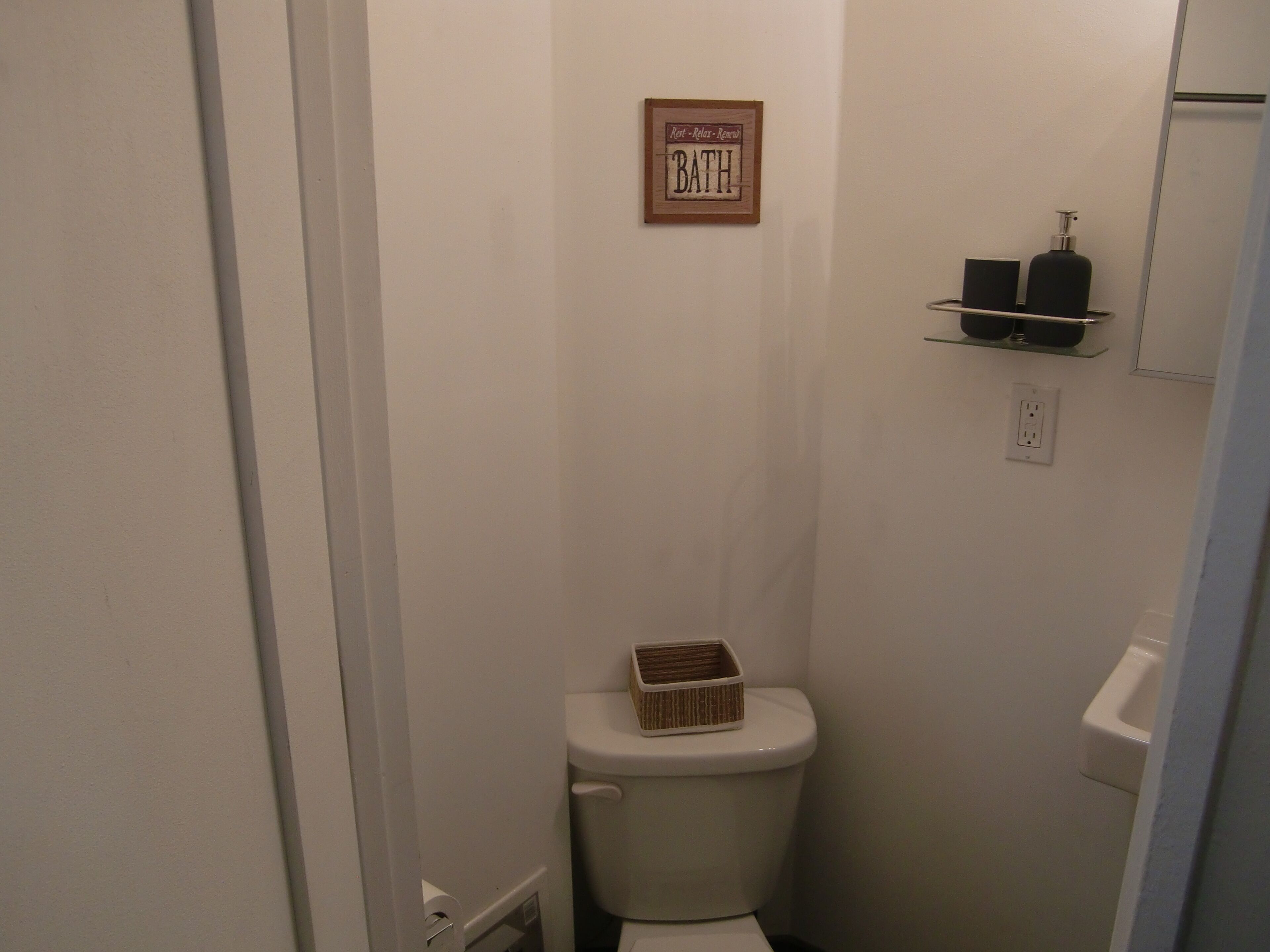 Un baño pequeño y funcional con un inodoro, un estante con artículos de aseo y un cartel sobre el inodoro.