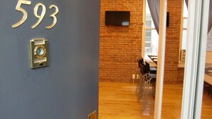 A room with a brick wall, a flat-screen TV mounted above a table, and a door with the number 593 on it. - Studios Midtown Manhattan (New York)