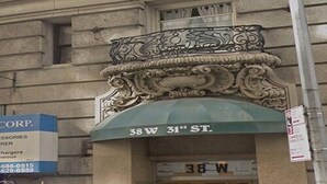A building with an ornate architectural detail above the entrance, a sign indicating '38 W 31st ST.', and a signboard for 'CORP. ACCESSORIES REFRIGERATORS'. - Studios Midtown Manhattan (New York)