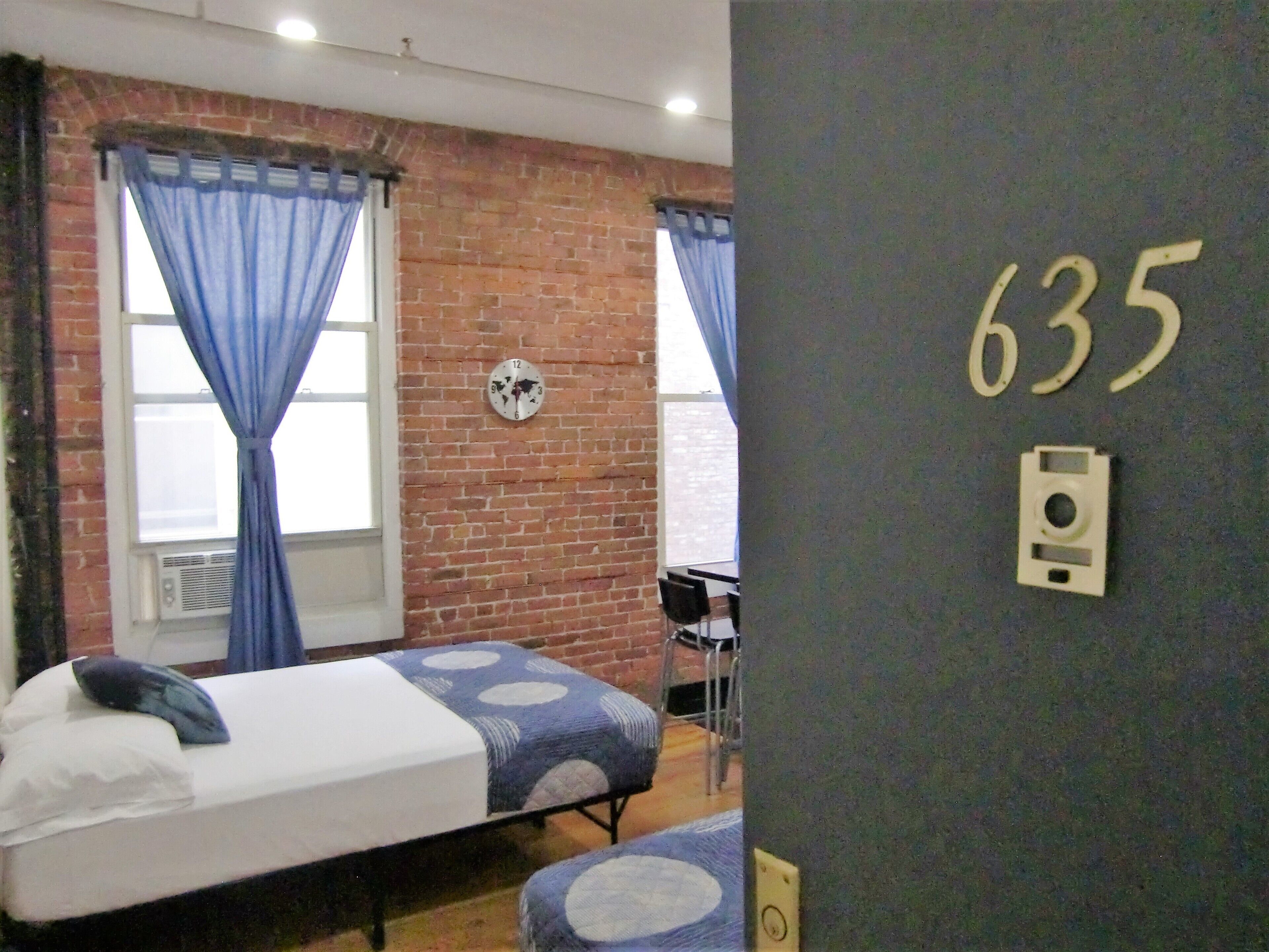 Una habitación con dos camas, una pared de ladrillo, un reloj y el número 635 en la pared.