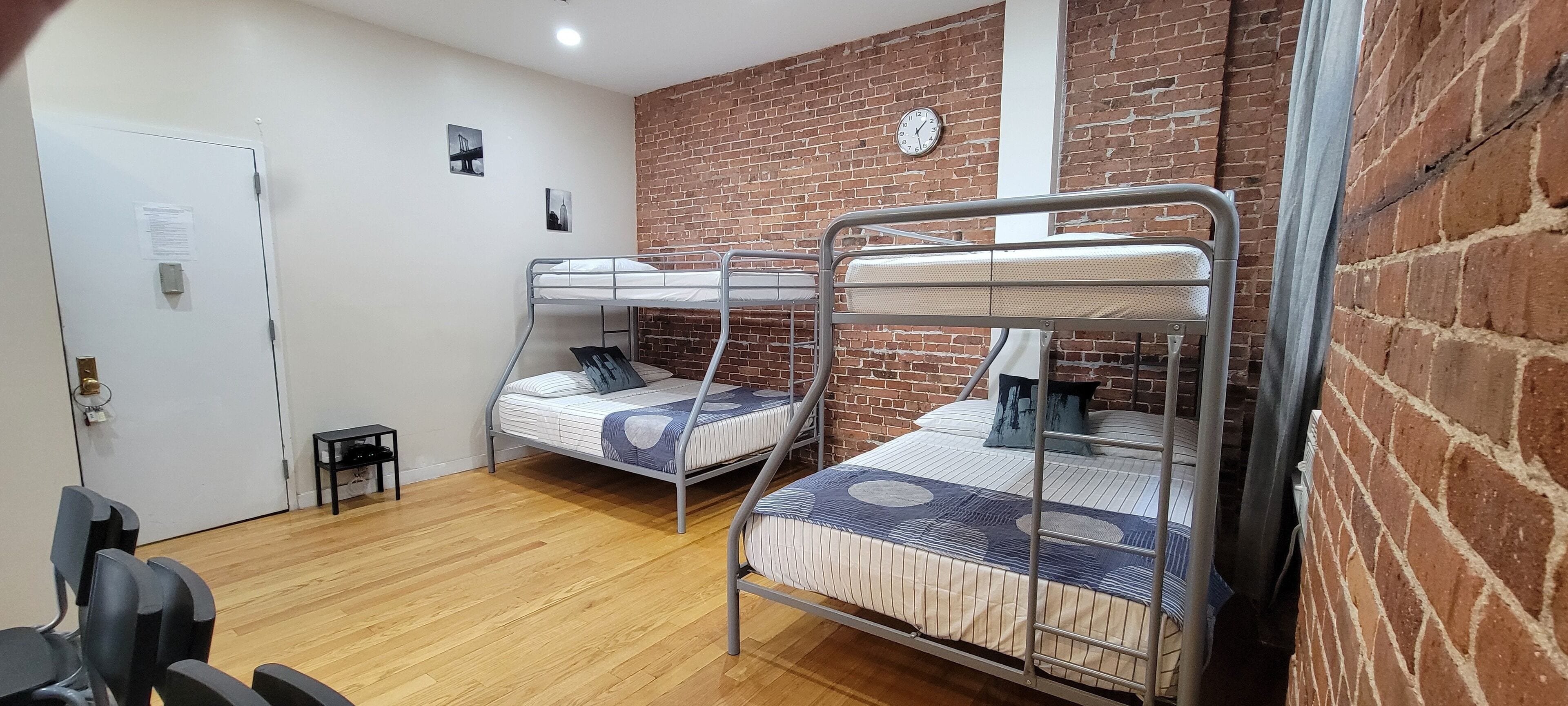 Un dormitorio con dos literas, suelo de madera, pared de ladrillo y una puerta con cerradura.