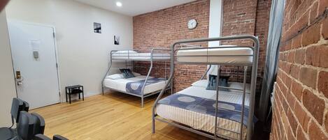 A dormitory room with two bunk beds, a wooden floor, a brick wall, and a door with a lock.