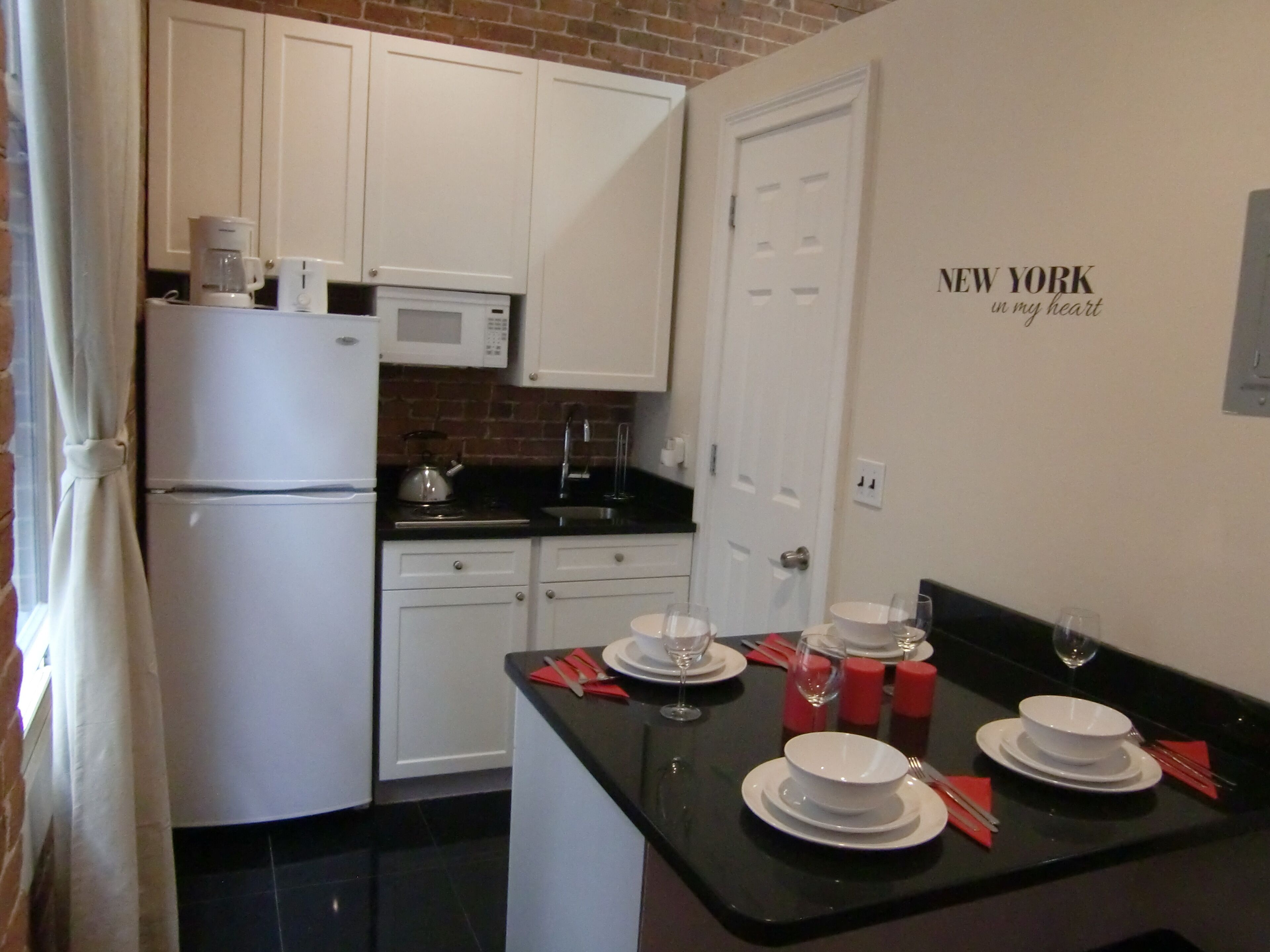 A modern kitchen with white cabinets, a black countertop, and a dining area set for four with white plates and red napkins.