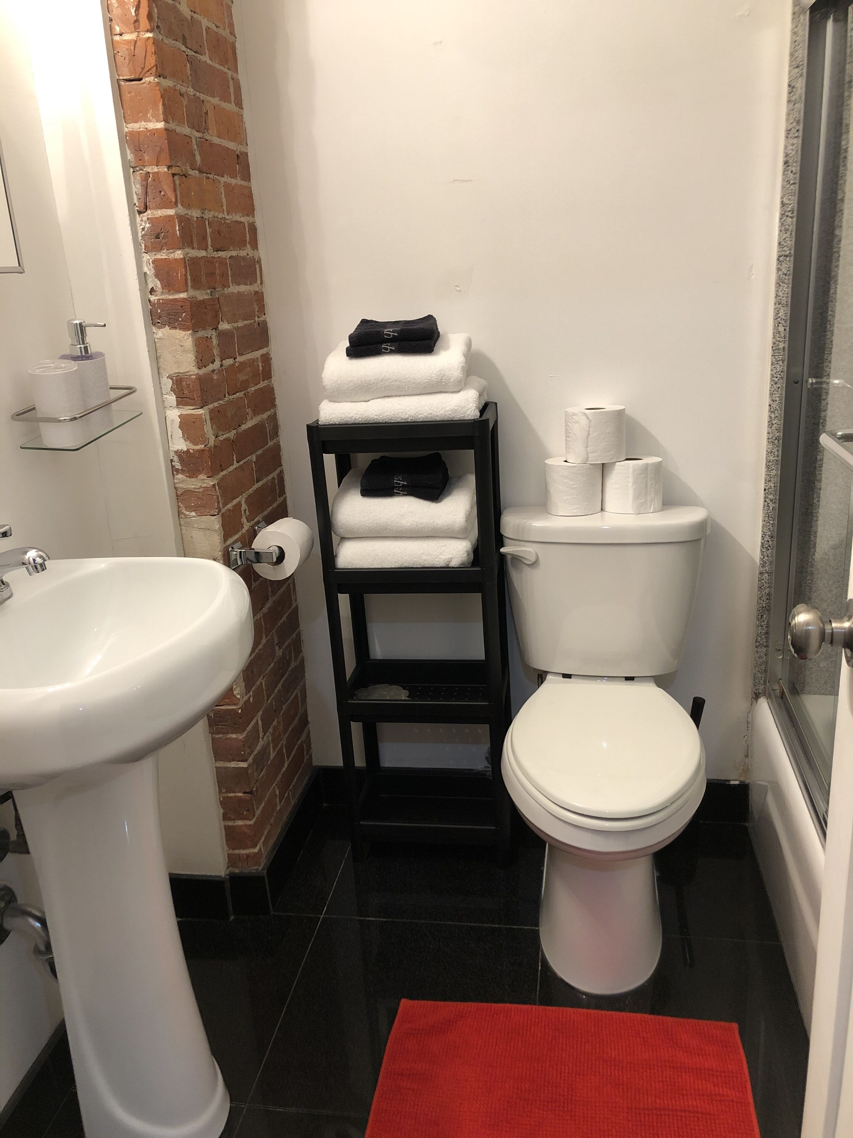 Un baño compacto con un lavamanos blanco, un inodoro y un estante pequeño con toallas.