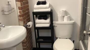 A compact bathroom with a white sink, a toilet, and a small shelf with towels.