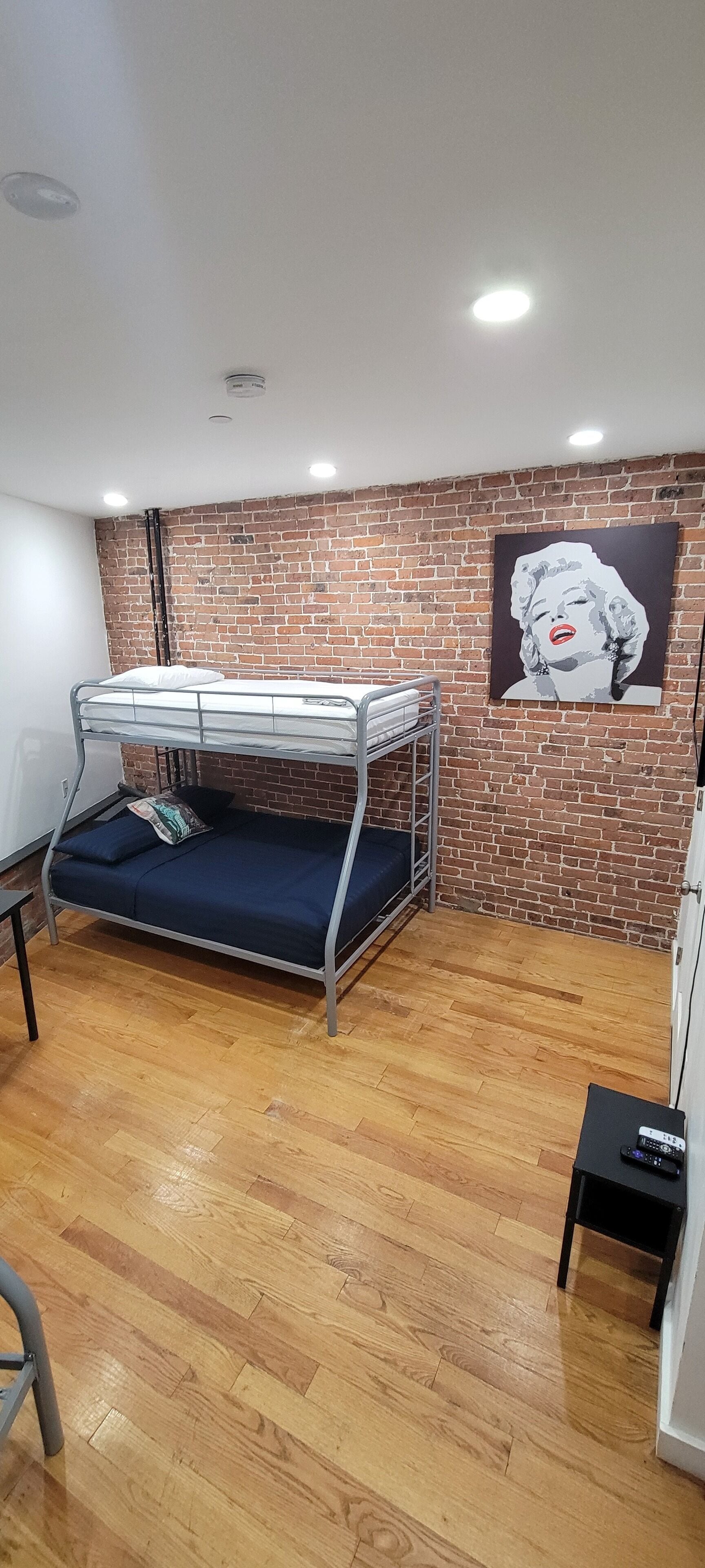 A bunk bed room with a brick wall, a poster, and a small table with a remote control.
